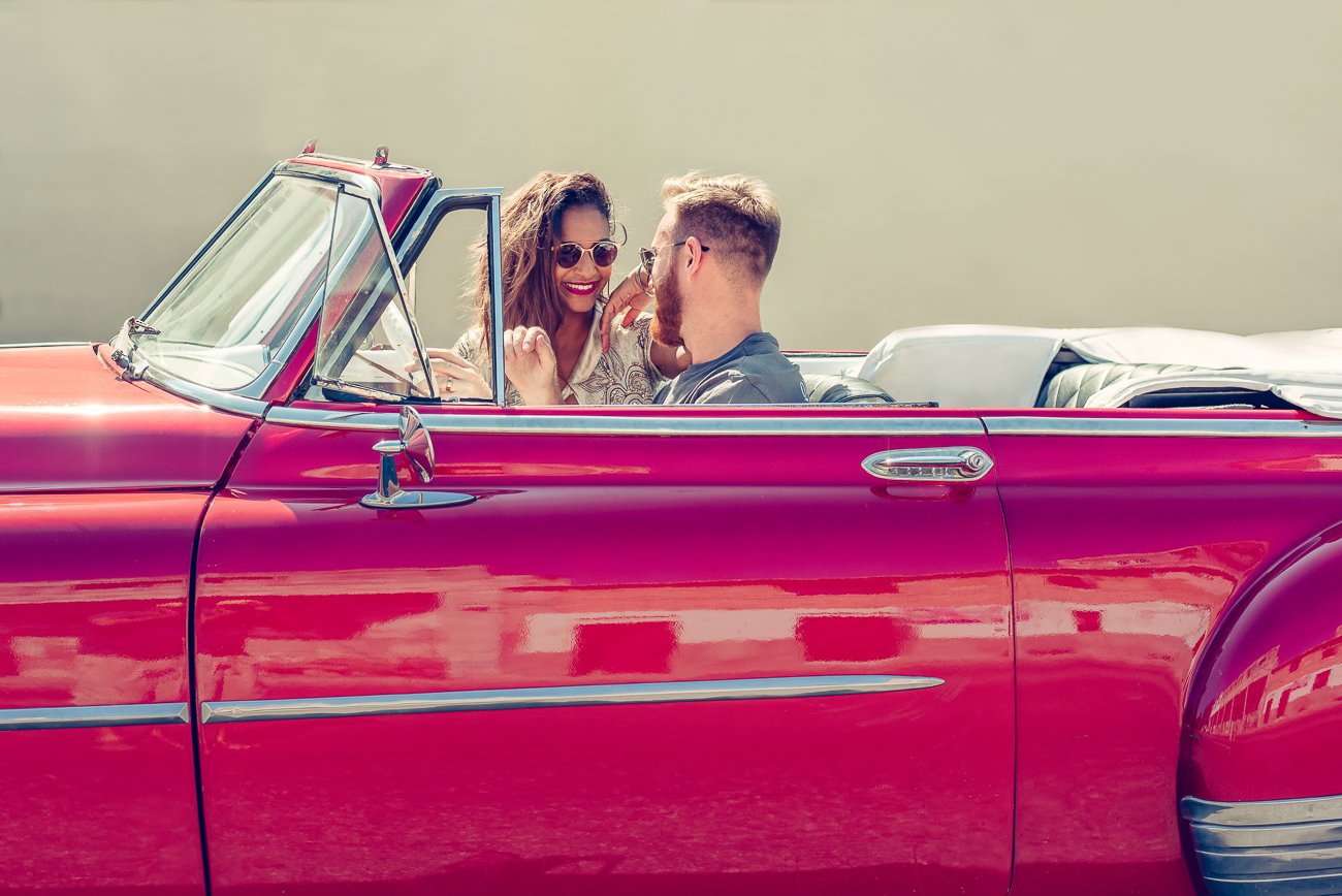 Engaged couple inside a vintage convertible car in Miami, smiling and looking at each other during their engagement photo session.
