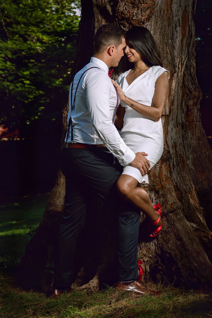 Bride leaning against a tree as the groom leans toward her in a romantic garden setting