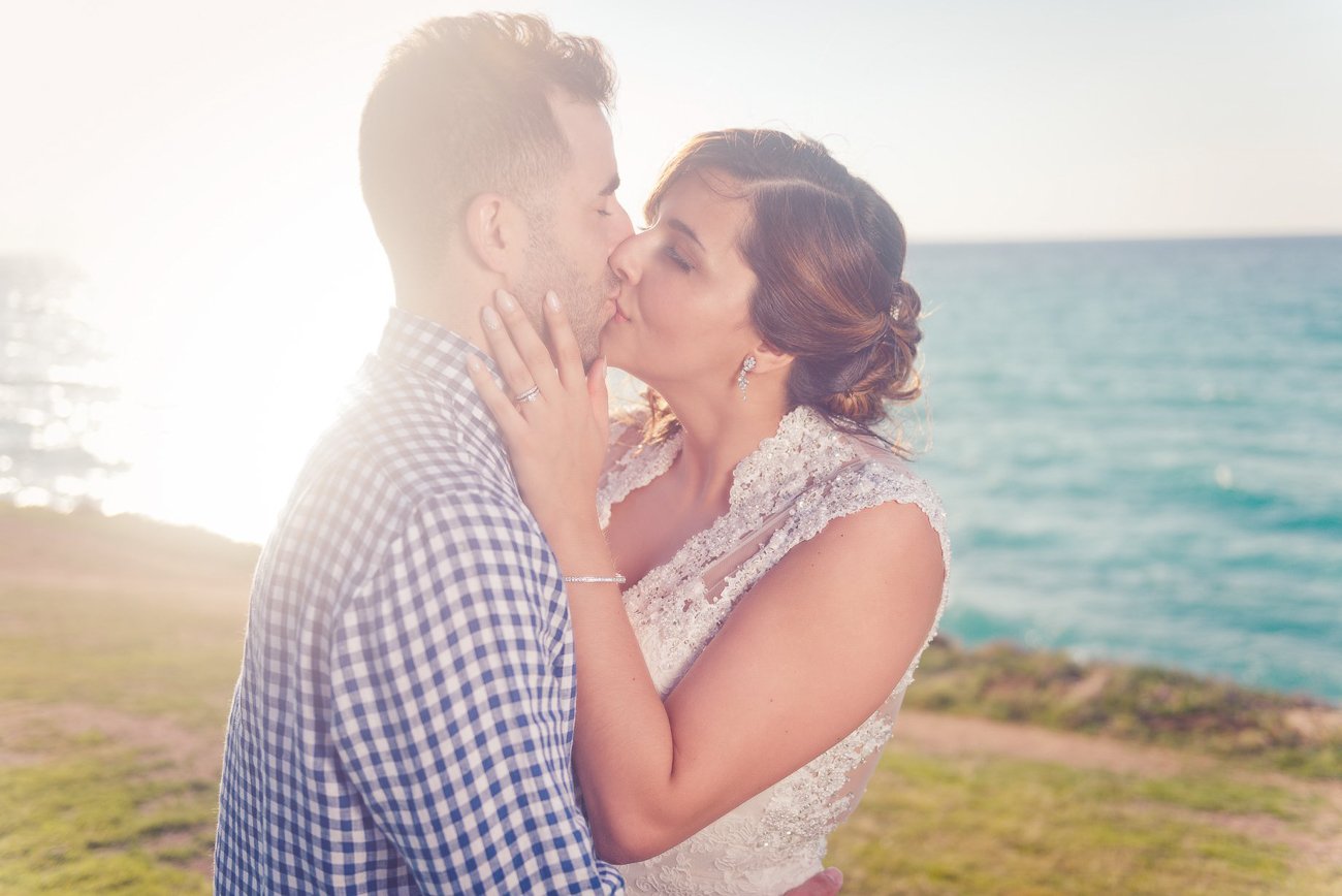 Wedding couple kissing with warm golden sunlight backlighting them, creating a soft halo — photographed by Alito Photography.