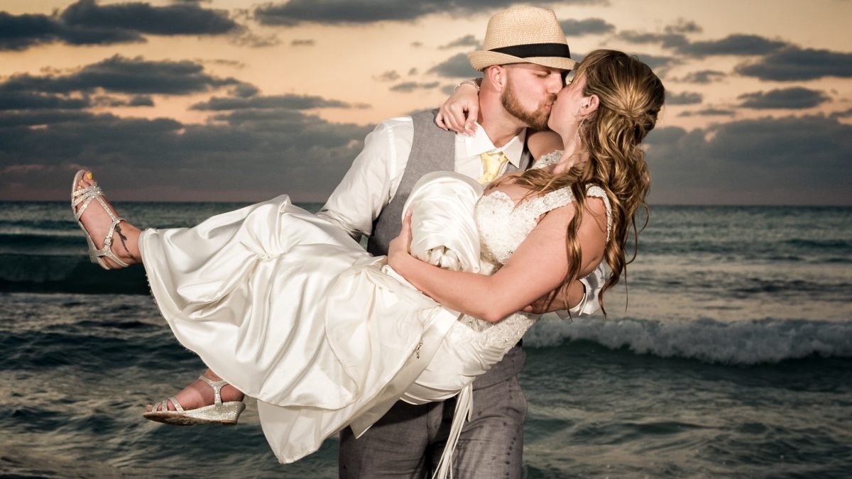 Groom kissing bride while carrying her in his arms at sunset on a Miami beach