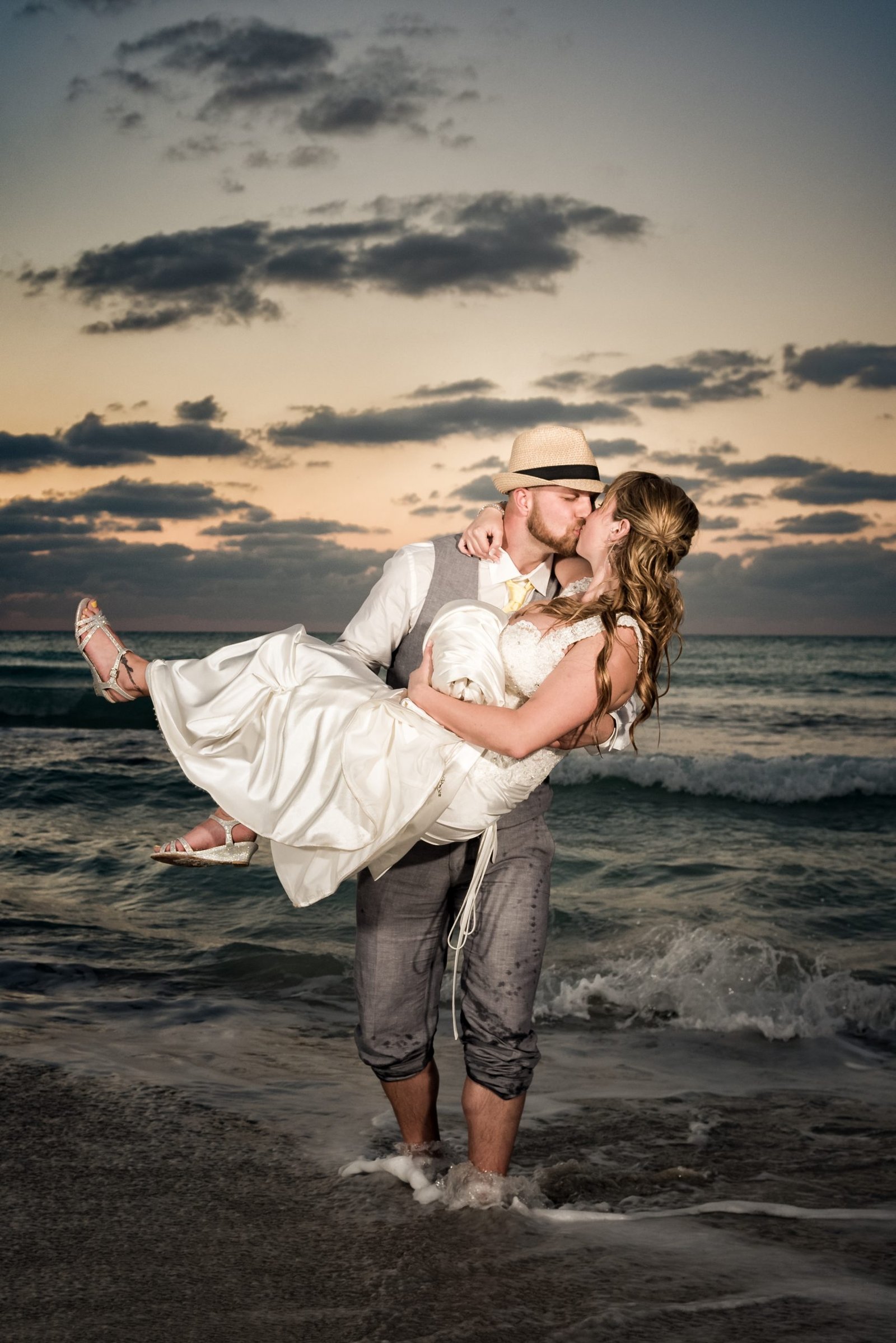 Groom kissing bride while carrying her in his arms at sunset on a Miami beach