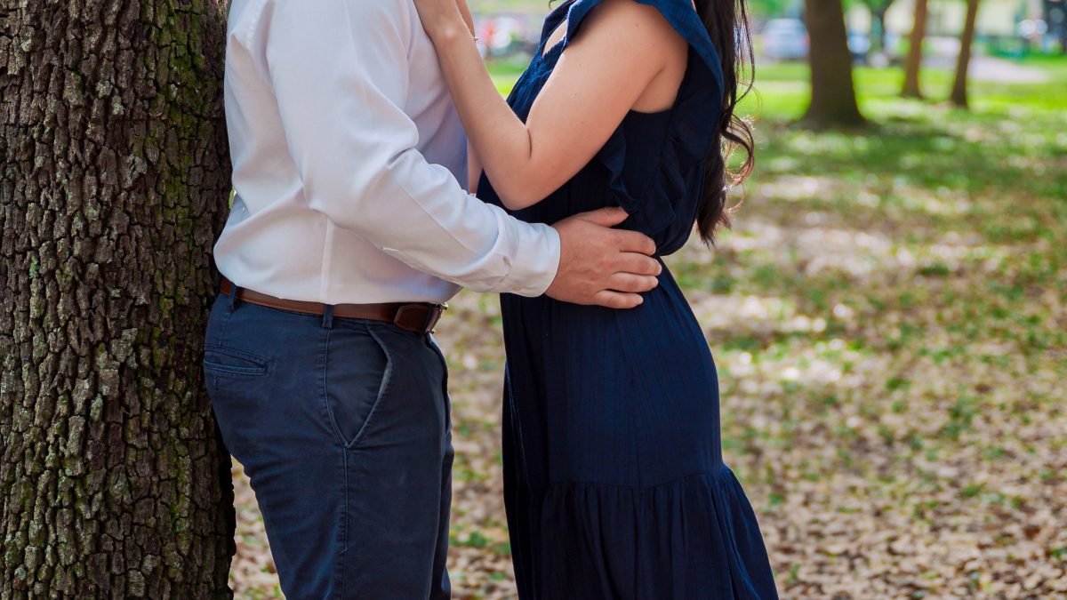 Engaged couple standing under a tree in a park, gazing into each other’s eyes