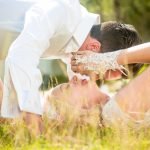 Romantic wedding photo of a bride and groom lying on the grass in their wedding attire, sharing an intimate, peaceful moment outdoors.