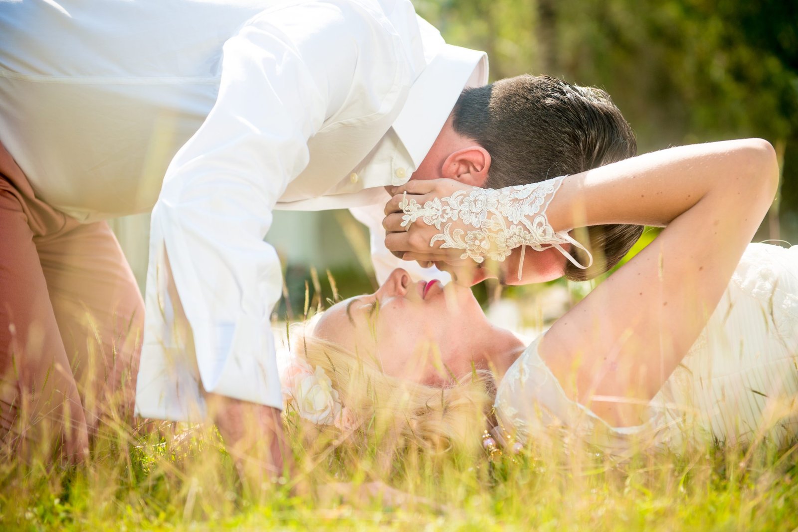 Romantic wedding photo of a bride and groom lying on the grass in their wedding attire, sharing an intimate, peaceful moment outdoors.