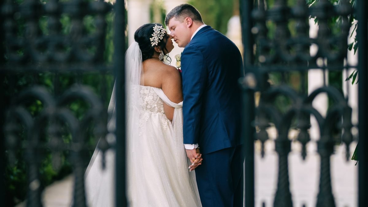 Wedding couple kissing by the wrought iron gate as they enter the venue garden.