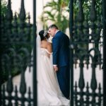 Wedding couple kissing by the wrought iron gate as they enter the venue garden.