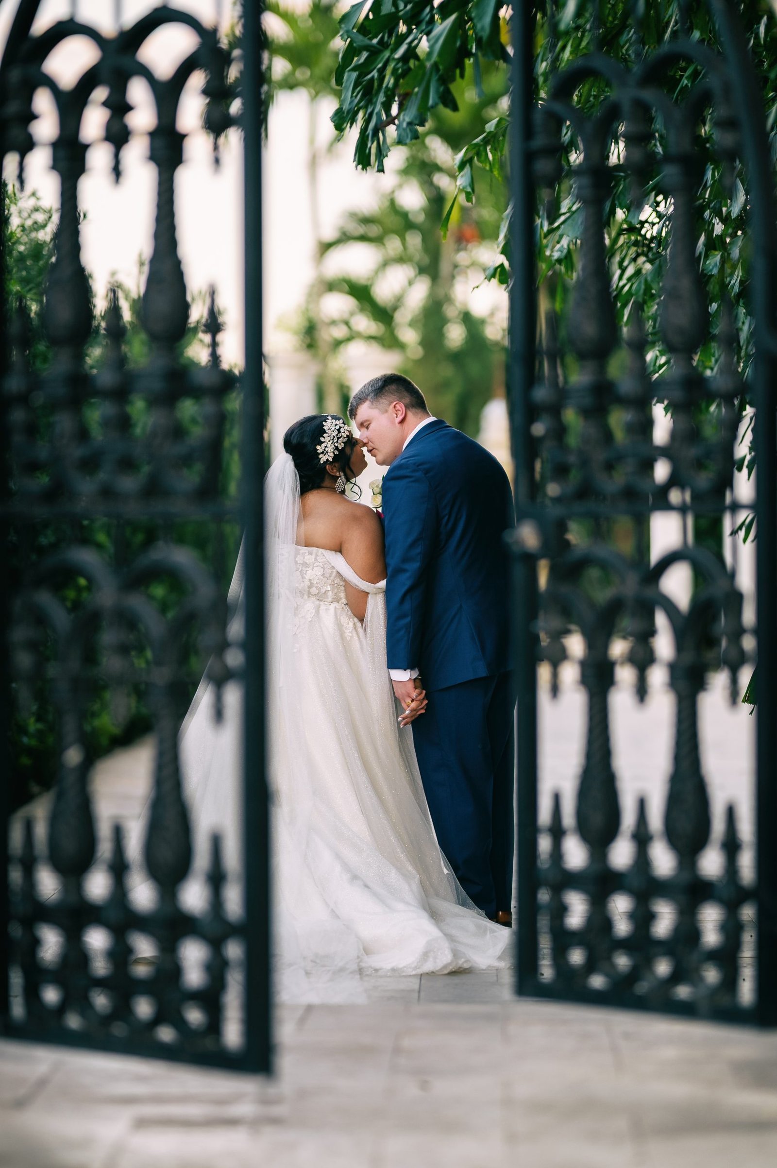 Wedding couple kissing by the wrought iron gate as they enter the venue garden.